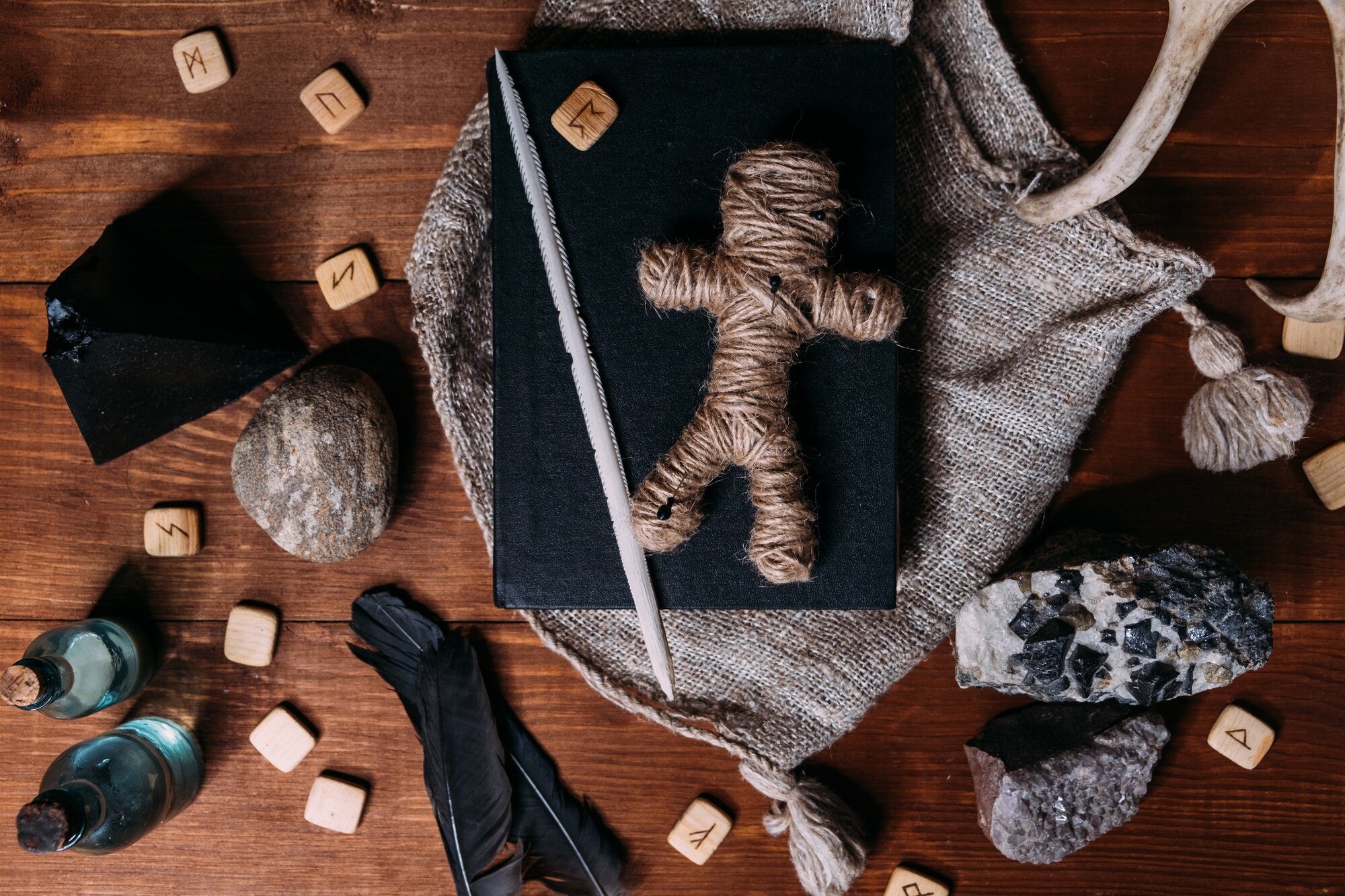 Lalka voodoo wykonana ze sznurka leży na czarnej książce, otoczona magicznymi przedmiotami rytualnymi, płasko leżąca