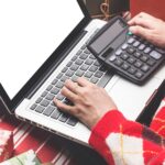 Świąteczne zakupy online. Kobieta kupująca z laptopem, przygotowująca się do wigilii, siedząca wśród pudełek i paczek z prezentami. Wyprzedaż ferii zimowych
