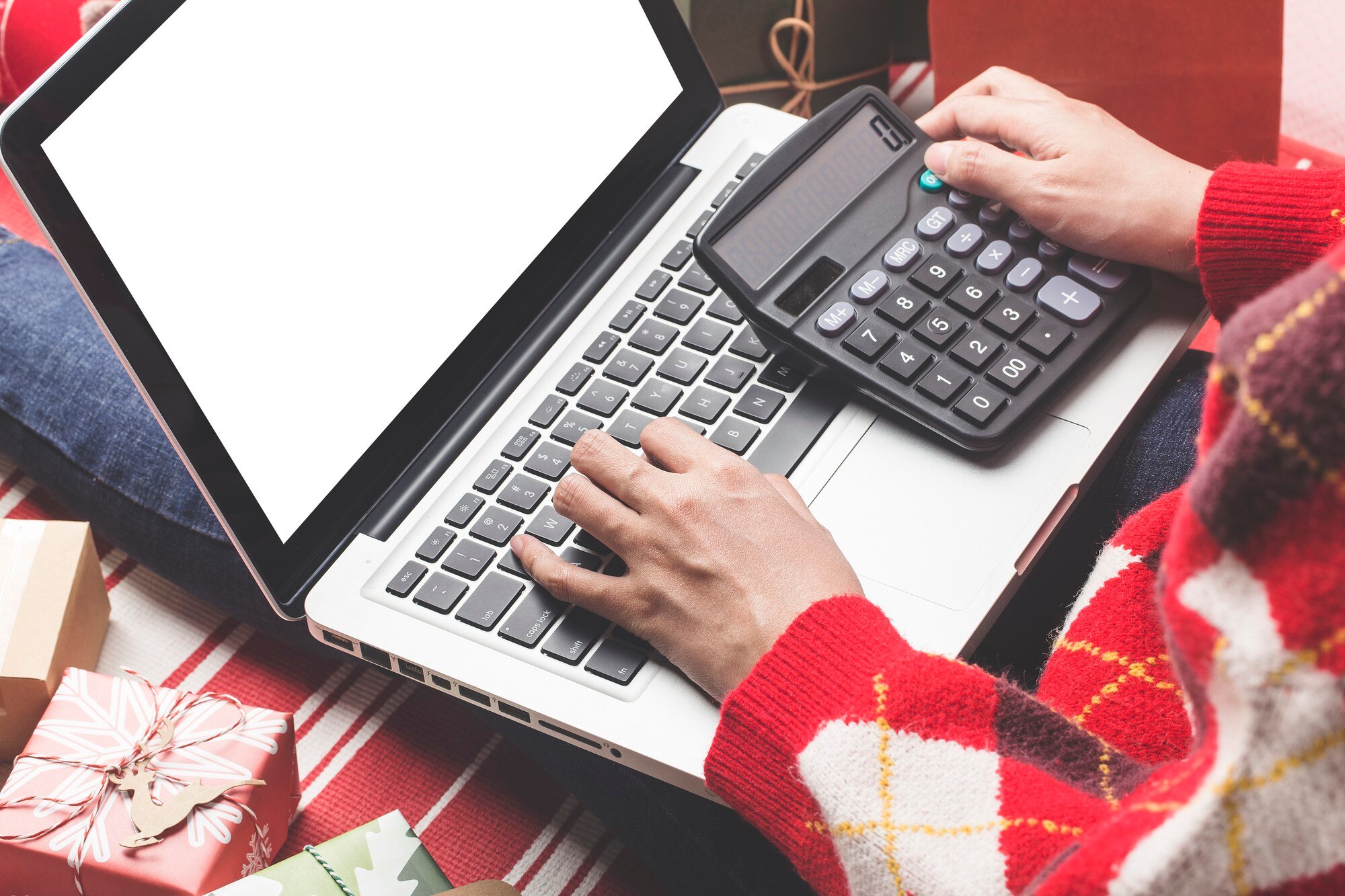 Świąteczne zakupy online. Kobieta kupująca z laptopem, przygotowująca się do wigilii, siedząca wśród pudełek i paczek z prezentami. Wyprzedaż ferii zimowych