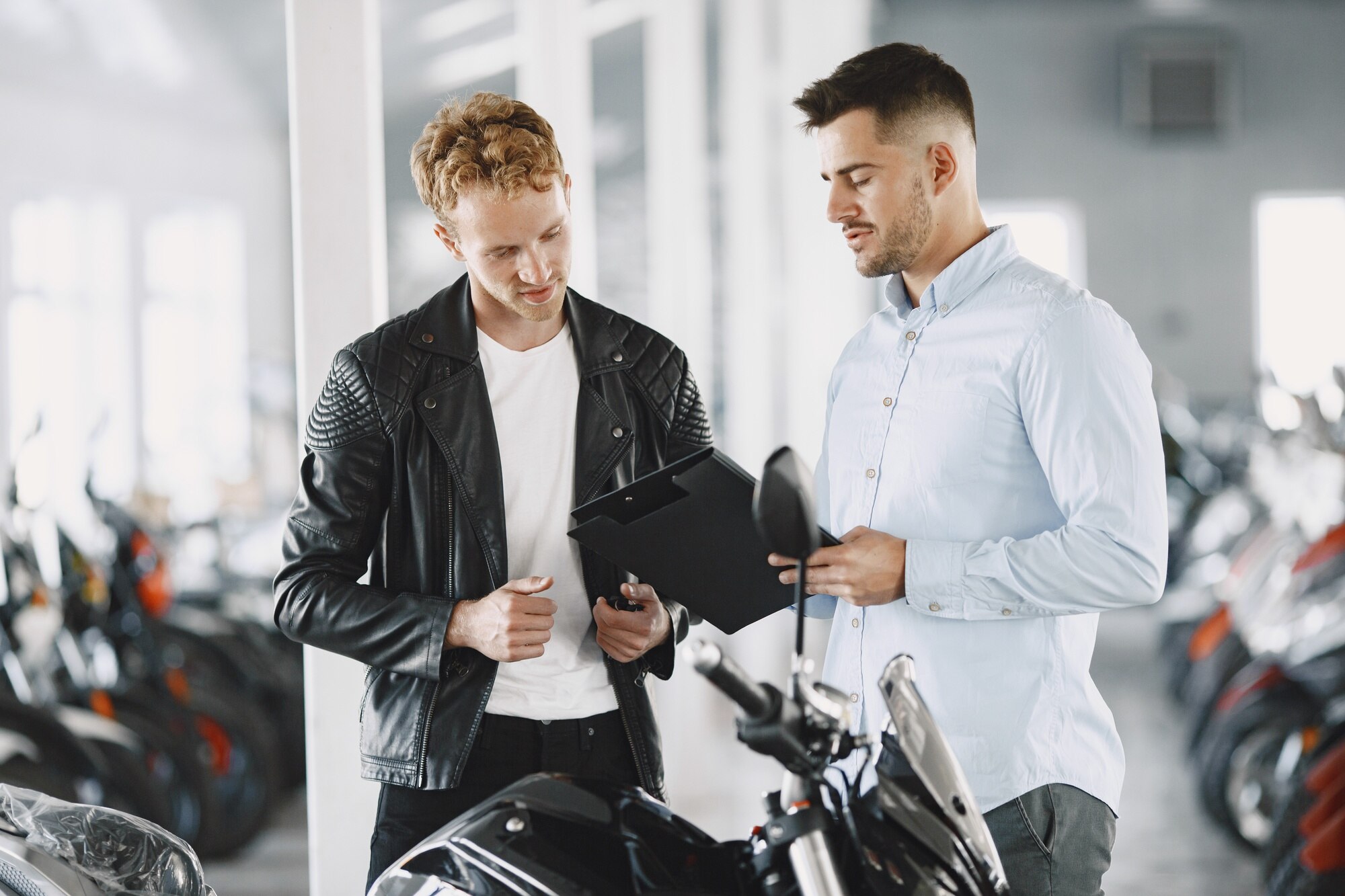 Mężczyzna wybrał motocykle w sklepie moto. Facet w czarnej kurtce. Manager z klientem.