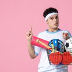 Widok z przodu młody mężczyzna w strojach sportowych z koszem pełnym rzeczy sportowych różową ścianą