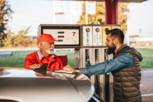 Młody przystojny dorosły mężczyzna wraz ze starszym pracownikiem stojącym na stacji benzynowej i tankowania samochodu.