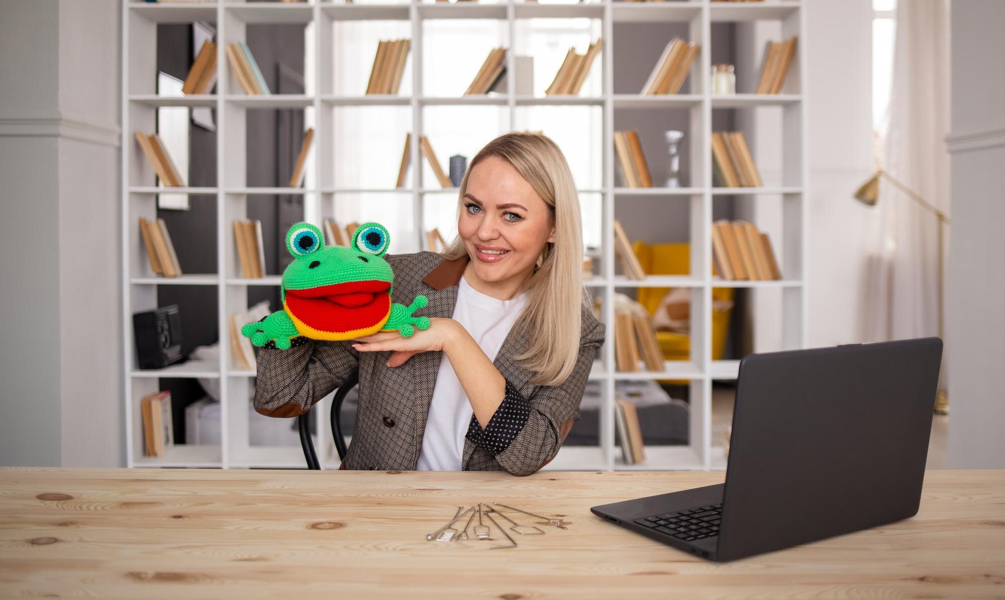 Terapeuta rasy kaukaskiej siedzi przy stole w pokoju z żabką i laptopem