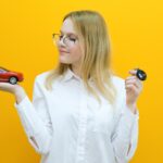 Piękna uśmiechnięta młoda kobieta z samochodem w dłoni Koncepcja nauki w szkole nauki jazdy i zakupu nowego samochodu na żółtym tle