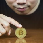 Bliska palec przytrzymaj bitcoina na stole z twarzą mężczyzny w tle