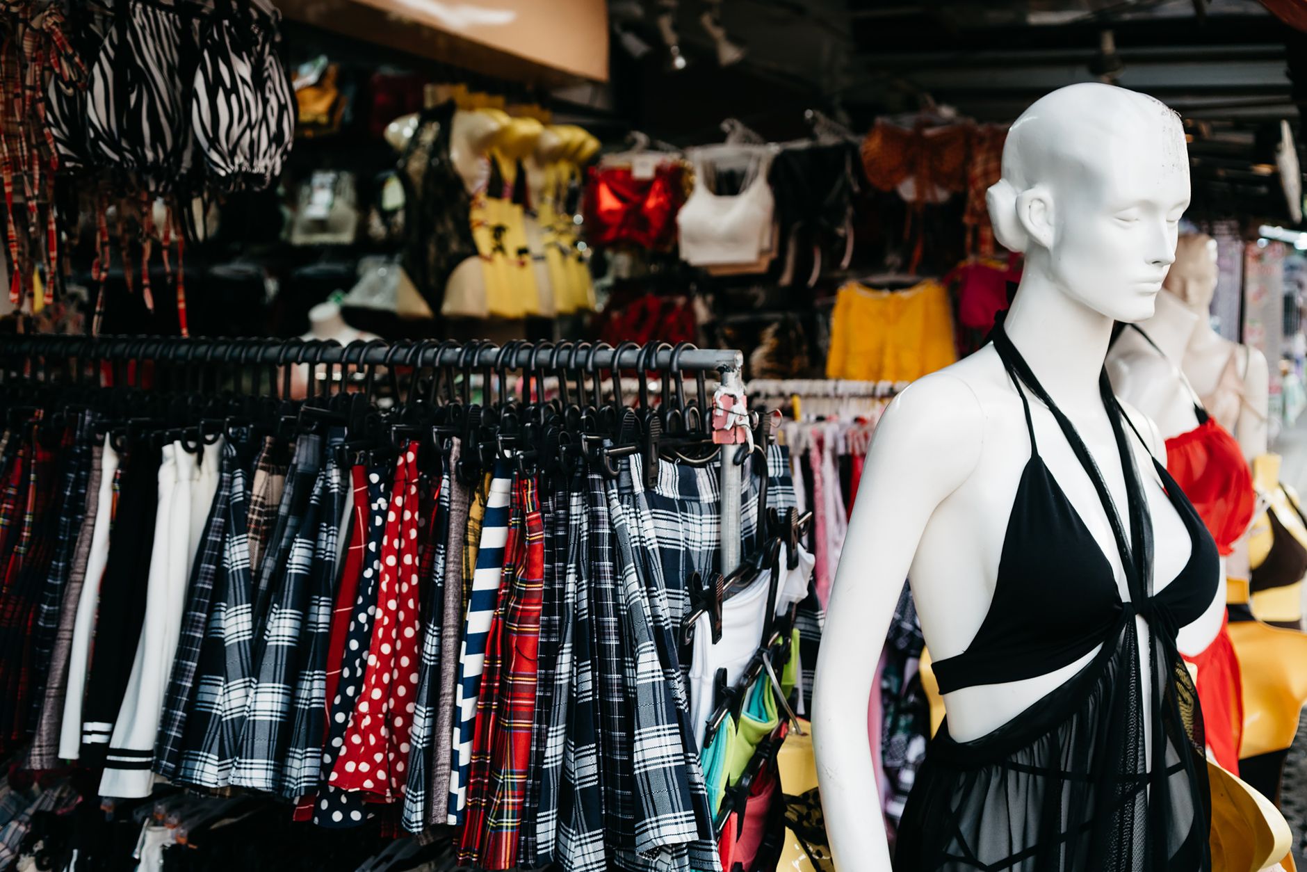 Vibrant market scene with a showcase of trendy clothing and a mannequin in an outdoor retail setting.