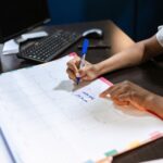 Person writing important notes in a desk calendar with a pen, set in an office.